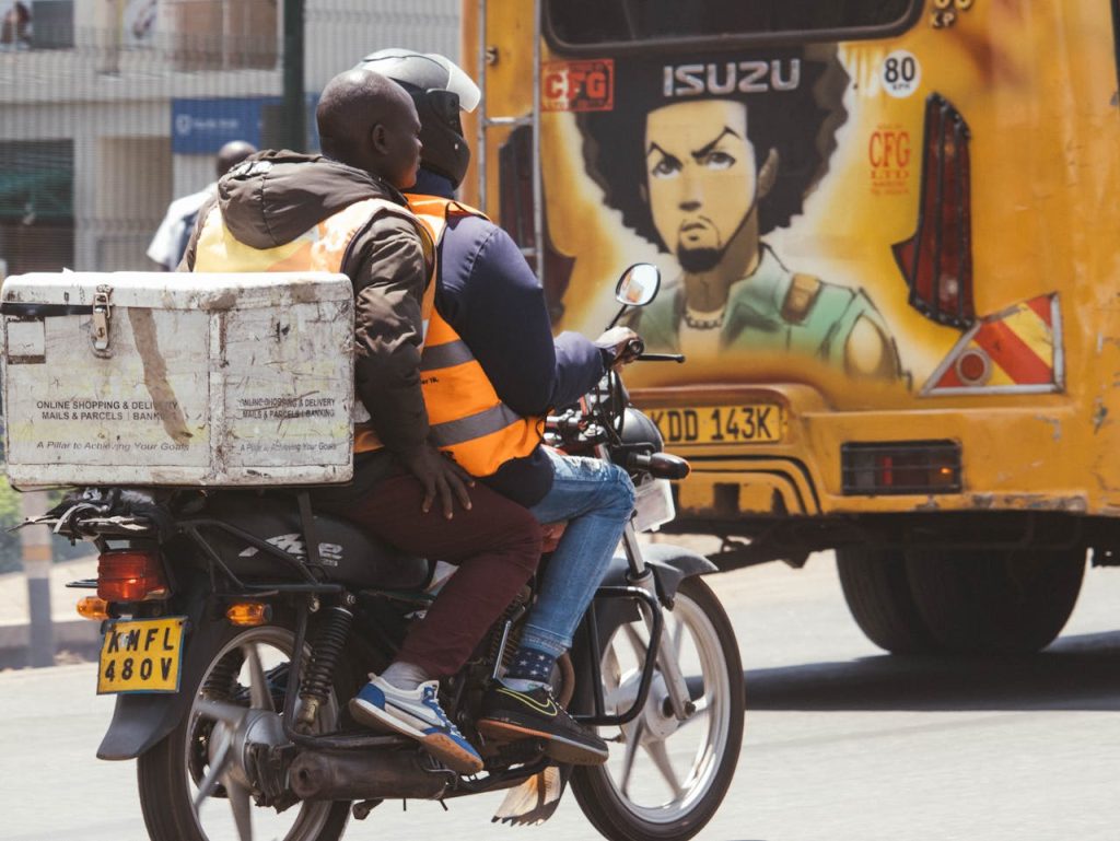 Motorcycle delivery service in Nairobi with vibrant street art in the background.