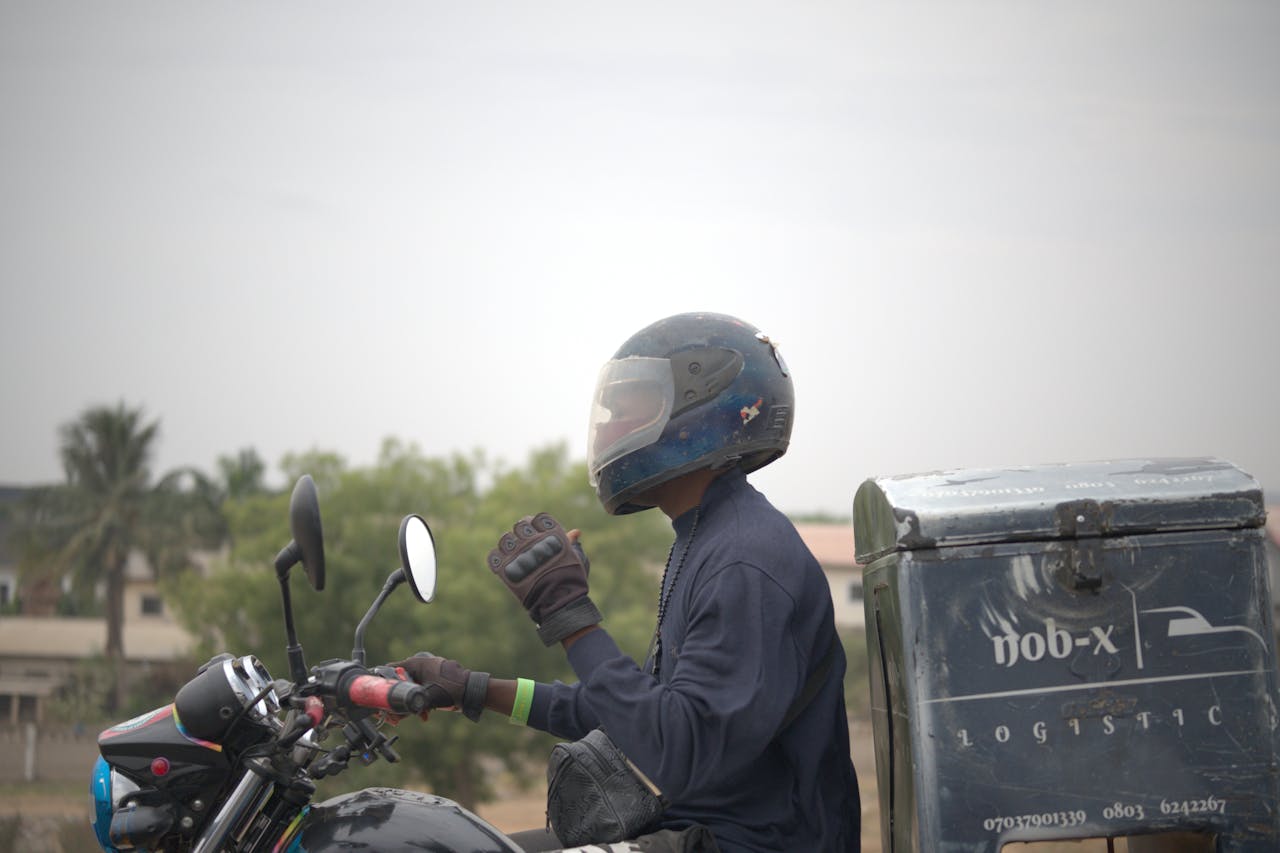 Delivery rider on a motorcycle in Nigeria, wearing protective gear and helmet.
