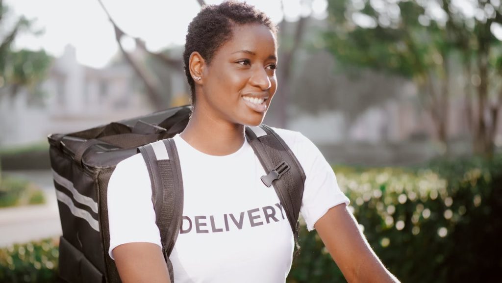 African American woman smiling with delivery backpack outdoors in daylight.